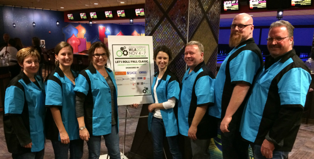 a team of seven WiLS members in cerulean blue bowling shirts pose around a poster board