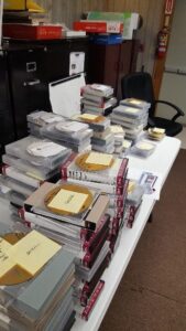 A long table in an office piled high with CD cases labelled with sticky notes.