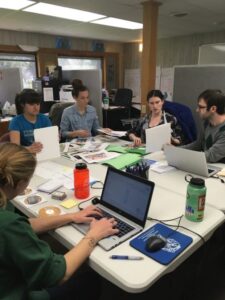 People in an office sitting around a table covered with paperwork